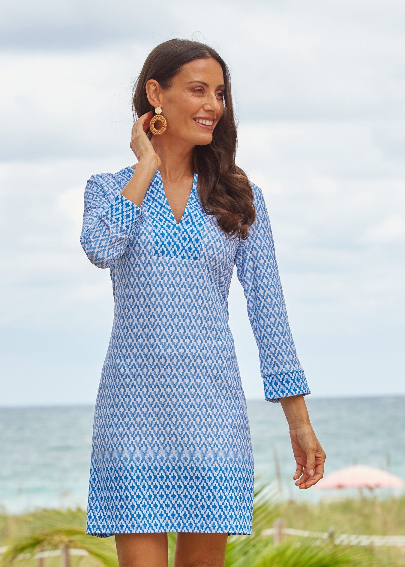 Woman wearing a blue patterned dress standing on a beach.