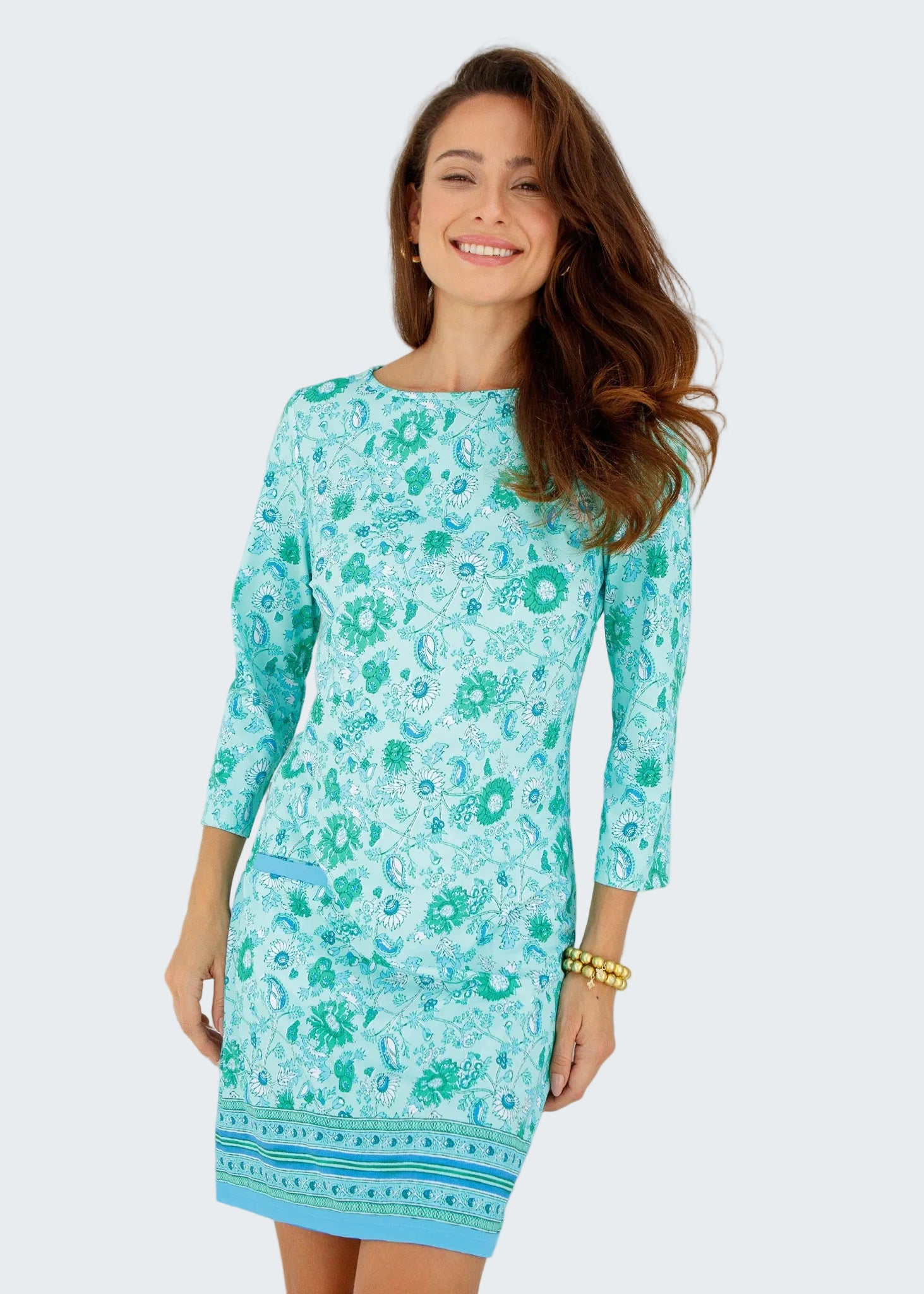 Woman wearing a turquoise floral dress standing in front of a white window.