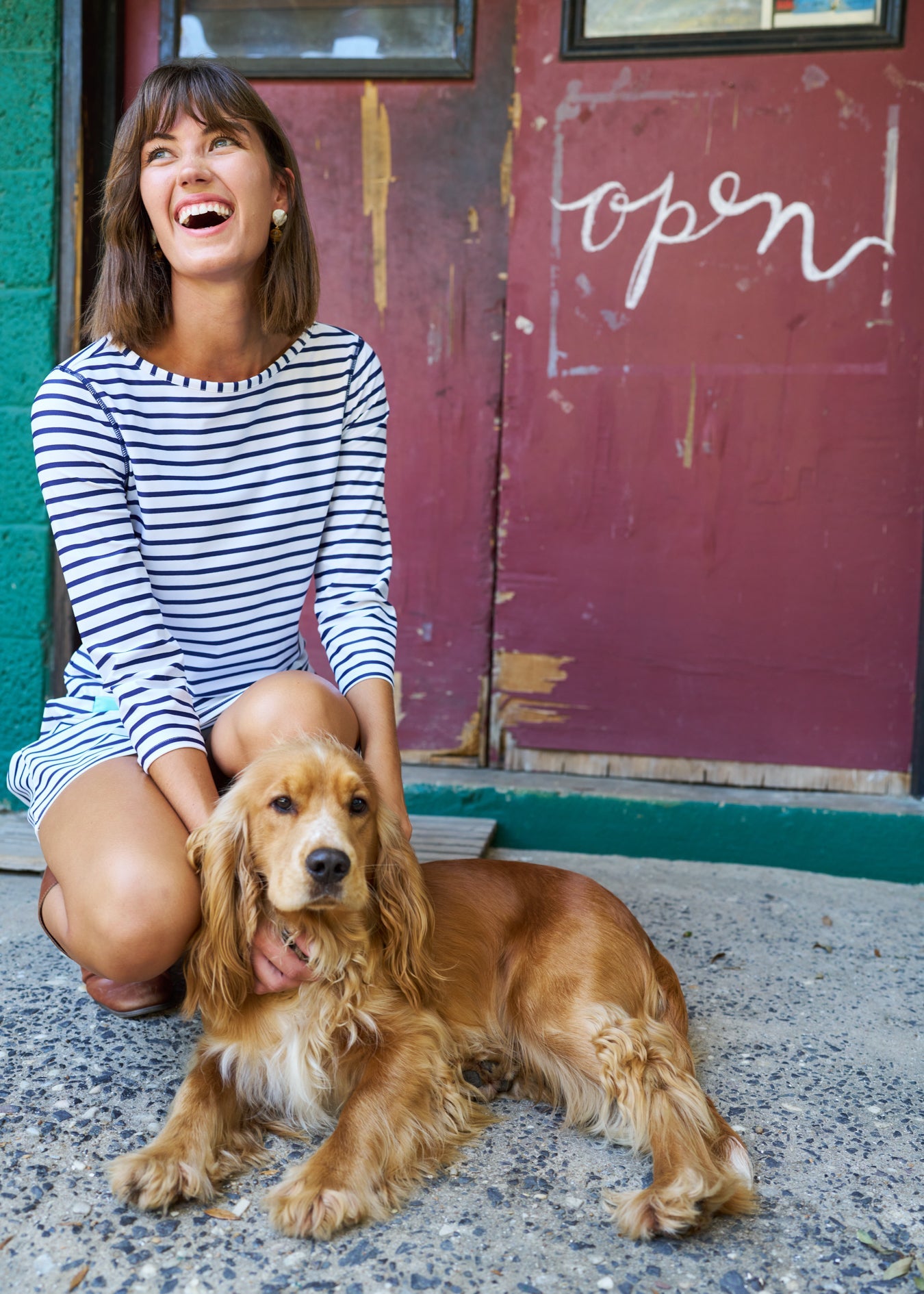Woman sitting with a dog in front of a door with 'open' written on it