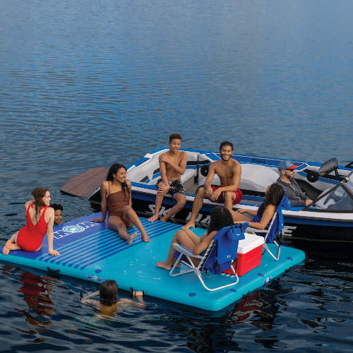 Group of people on a blue inflatable raft in the water with a boat in the background.