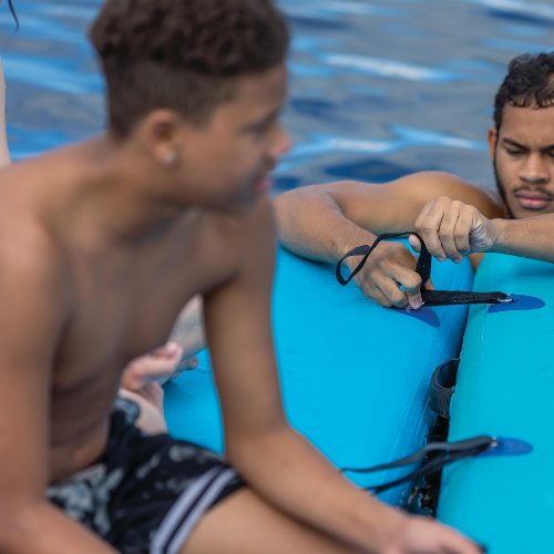 Two men sitting on blue floaties by a pool