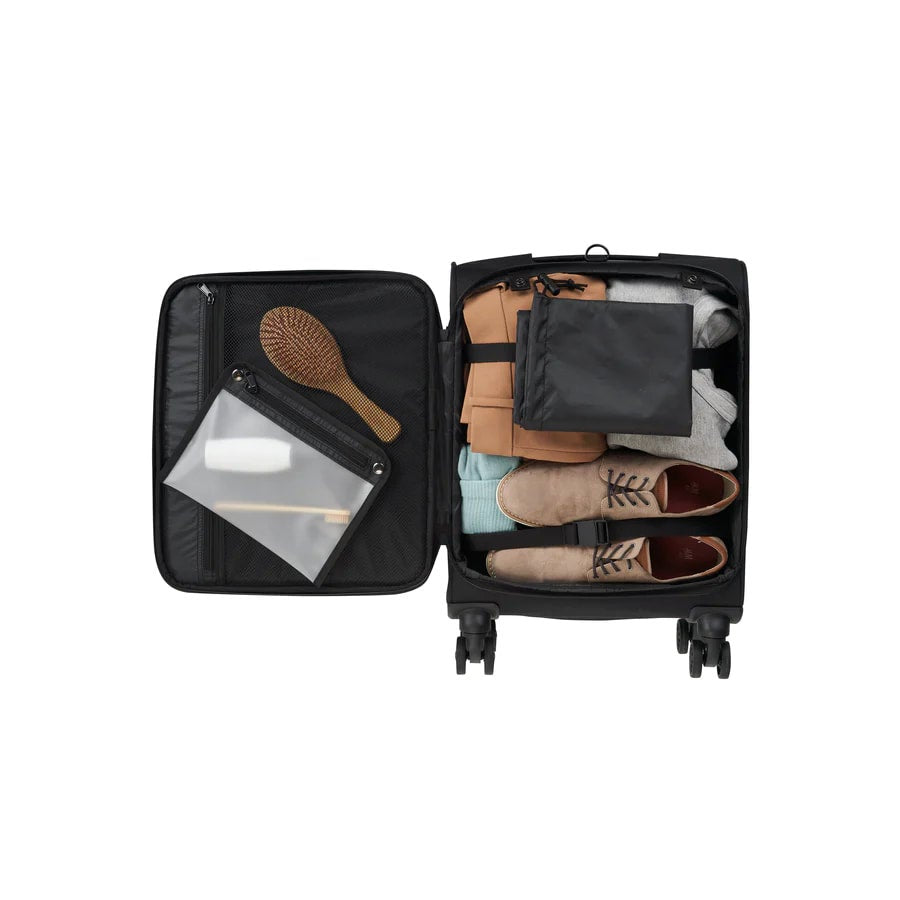 Open suitcase with travel items including shoes, a brush, and clothes on a white background