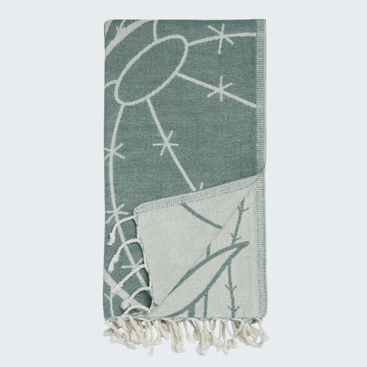 Teal towel with white geometric pattern and tassels on a white background