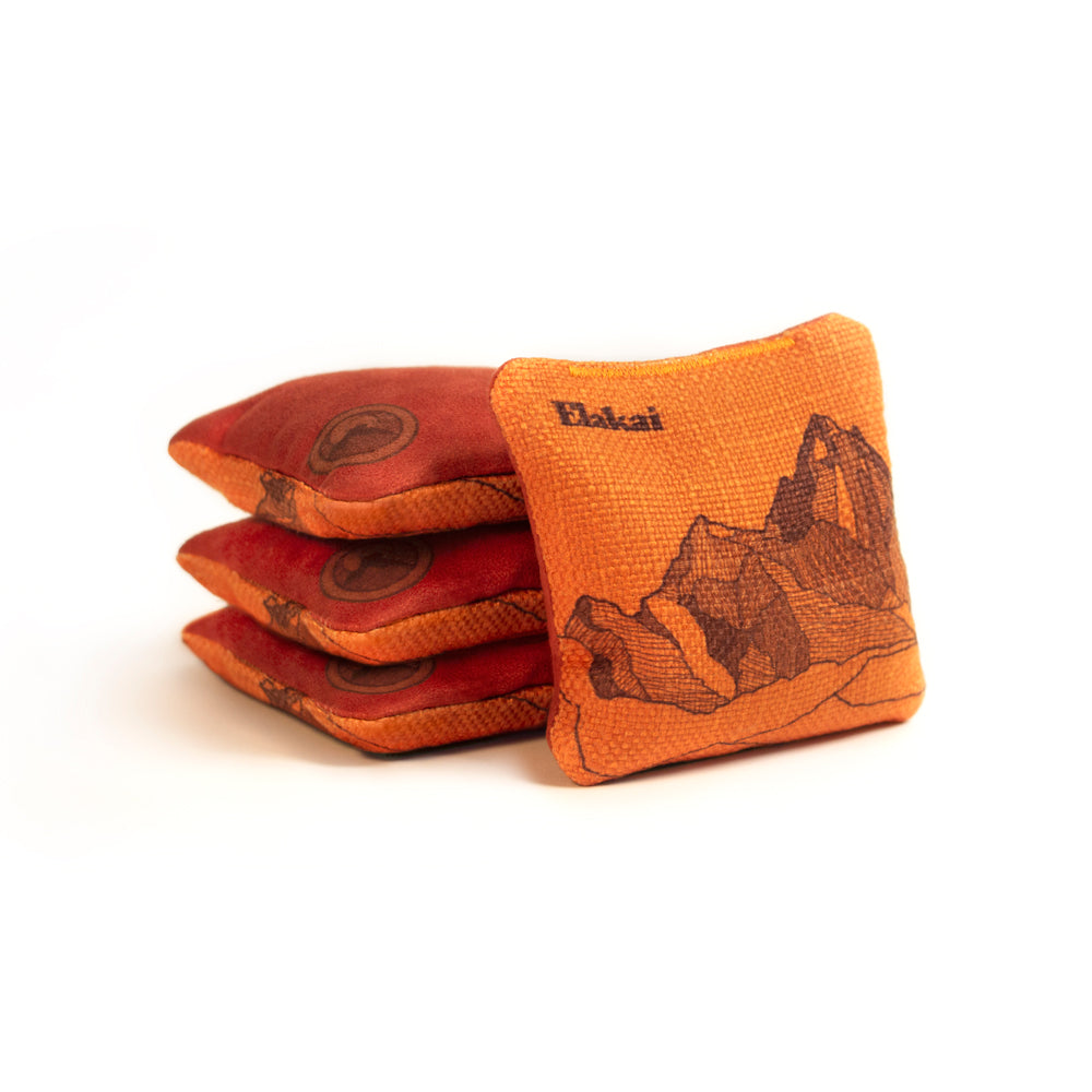 Stack of orange and red cornhole bags with a mountain design on a white background