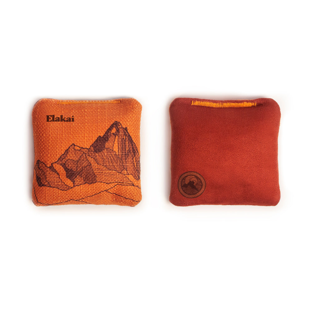 Two bean bags, one orange with a mountain design and Elakai branding, the other red with a logo, on a white background.