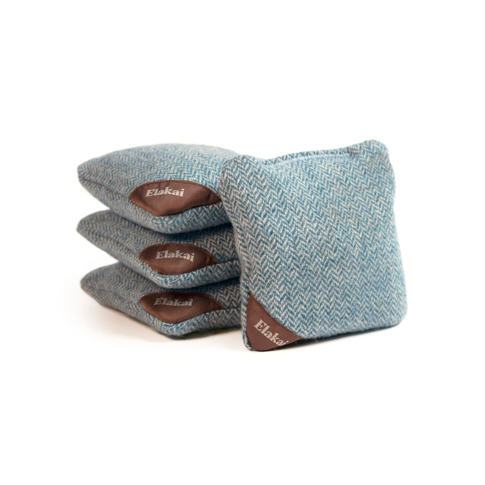 Four blue cornhole bags with brown leather handles on a white background