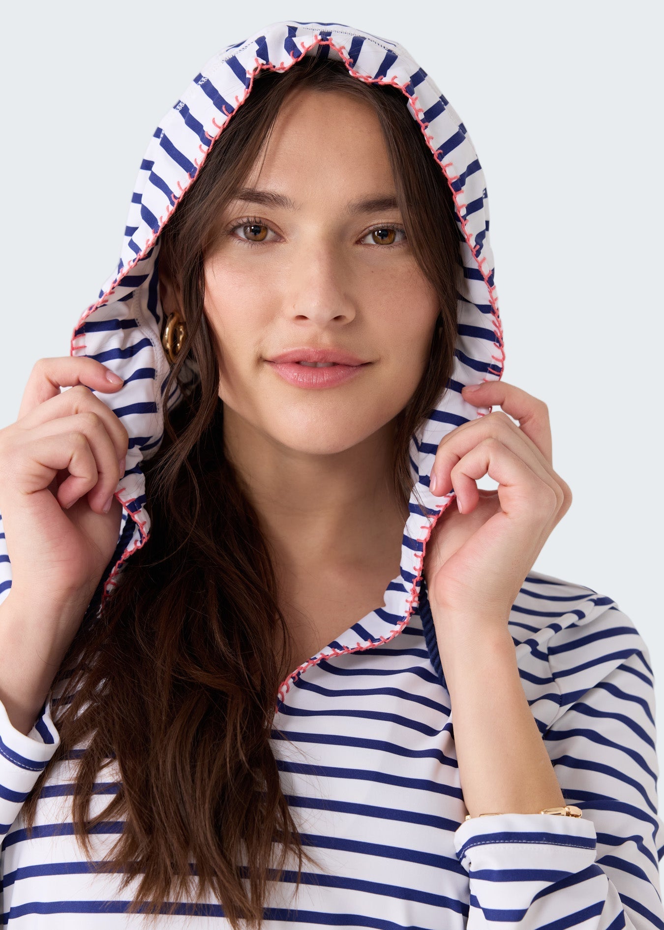 Woman wearing a blue and white striped hoodie with a hood on a light gray background