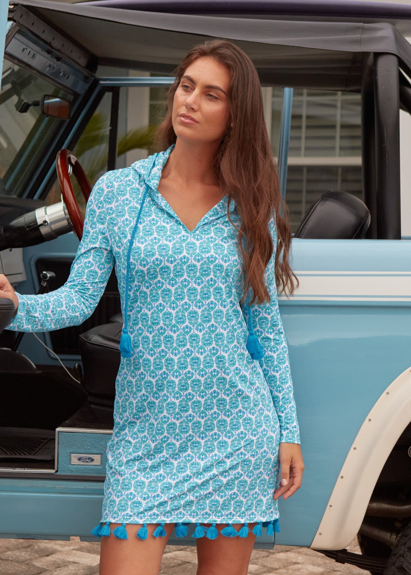Woman in a blue patterned dress standing next to a vintage vehicle