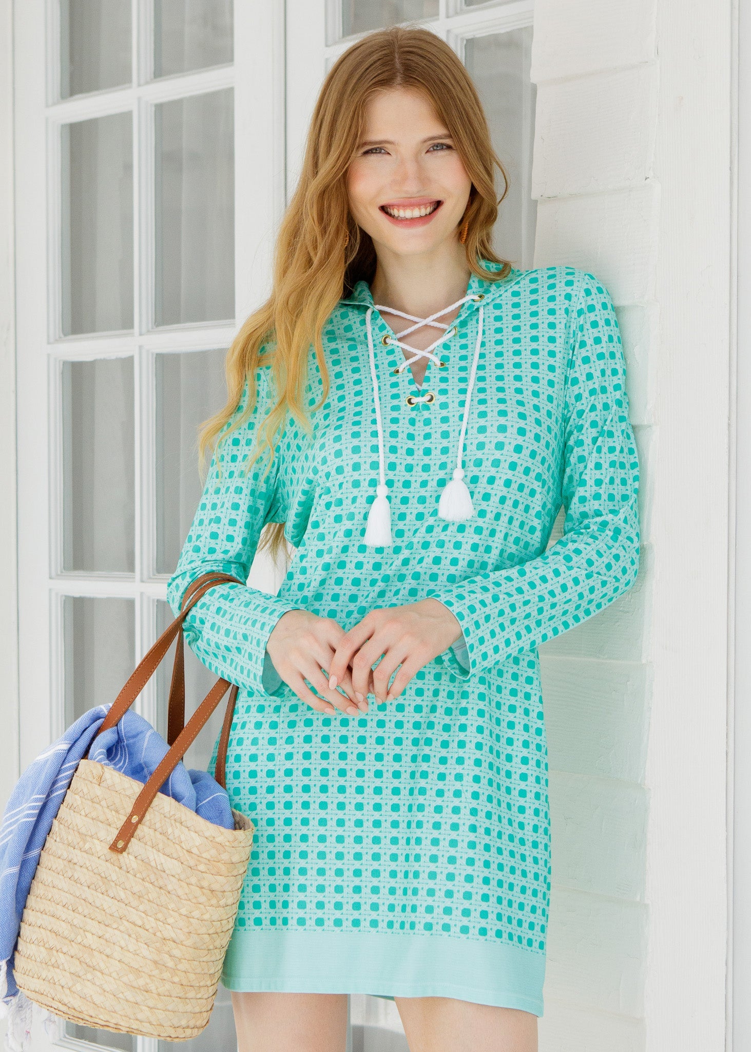 Woman wearing a turquoise checkered dress holding a straw bag indoors.