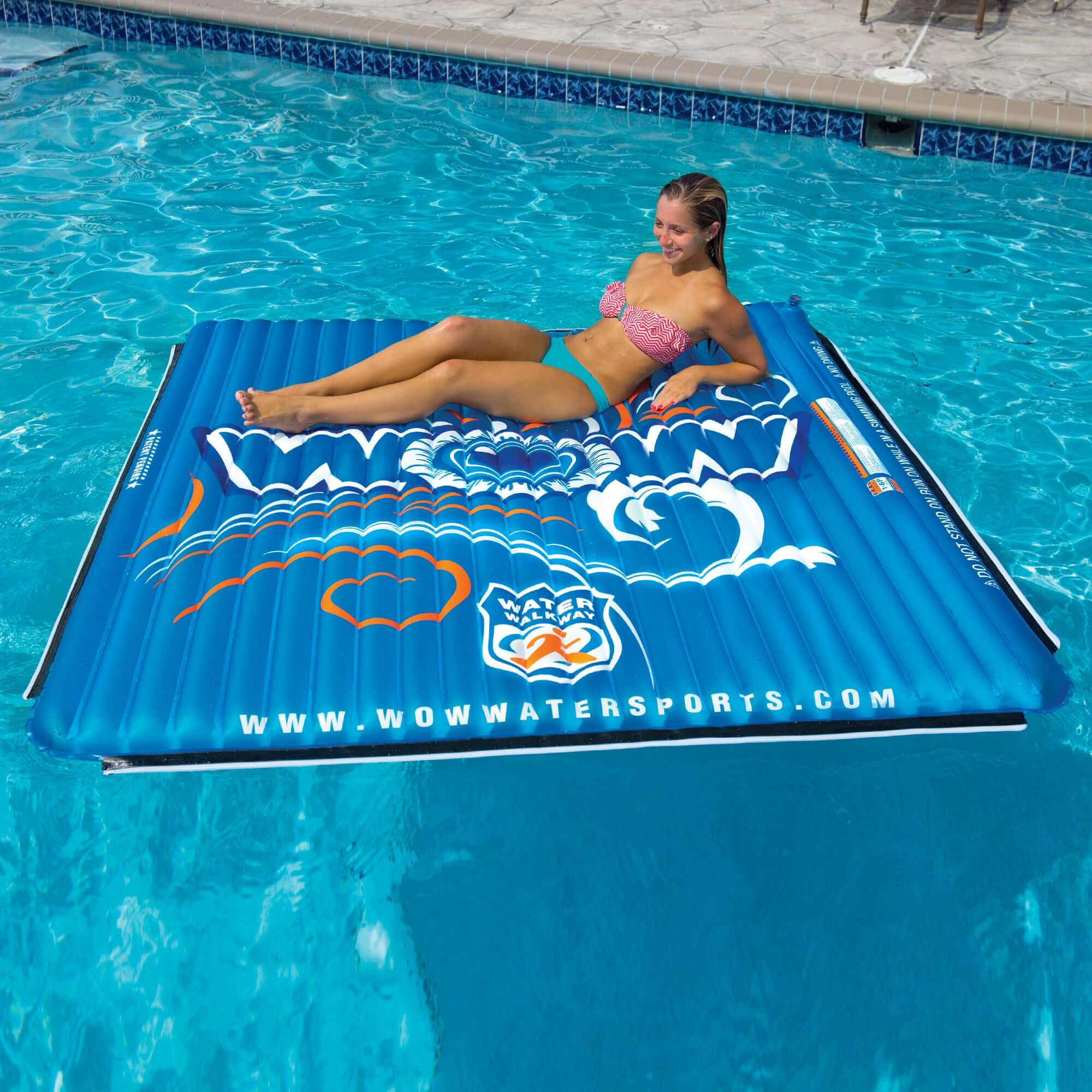 Woman lying on a blue inflatable pool mat with a visible brand logo in a swimming pool.