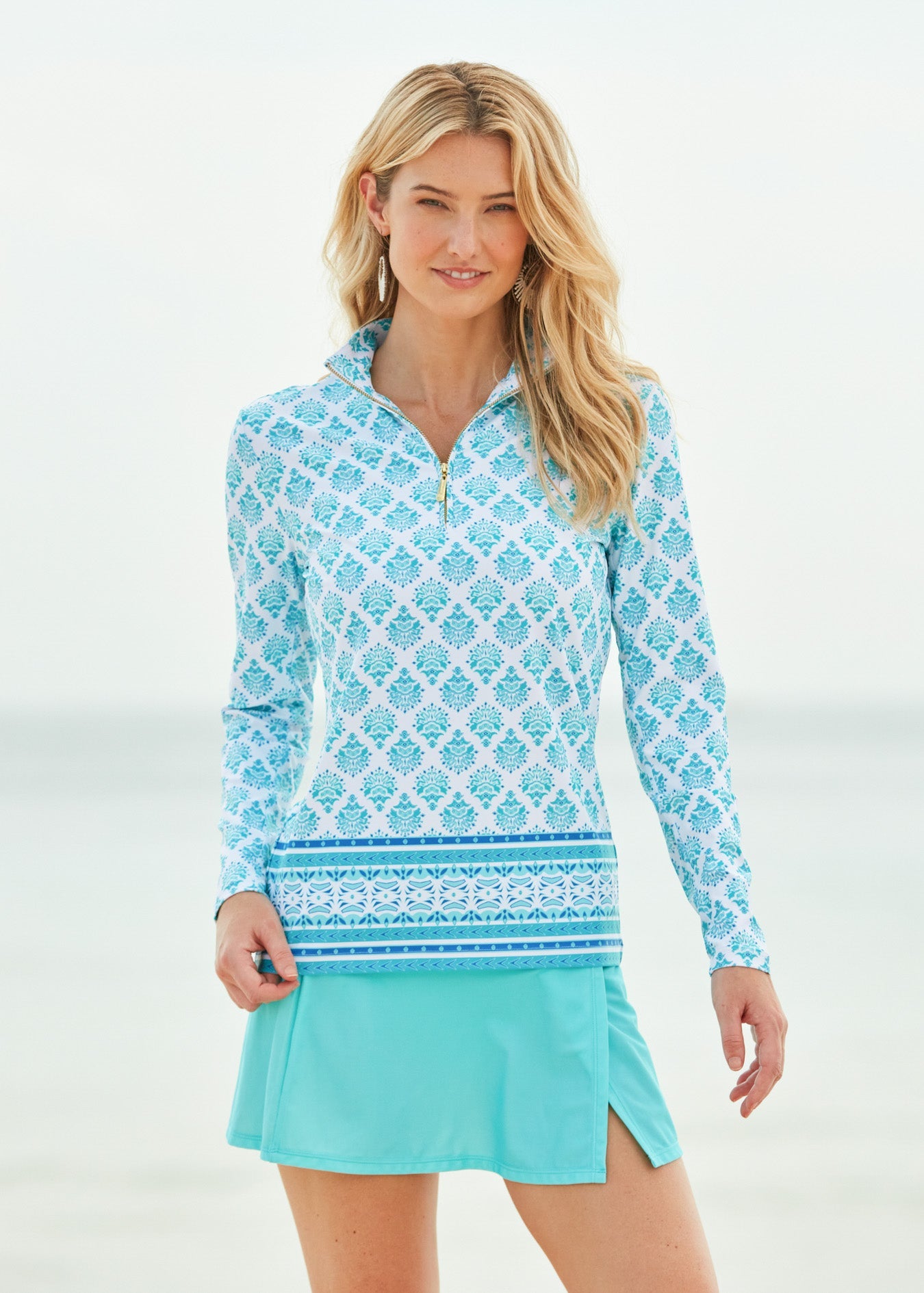 Woman wearing a patterned long-sleeve top and turquoise skirt on a white background