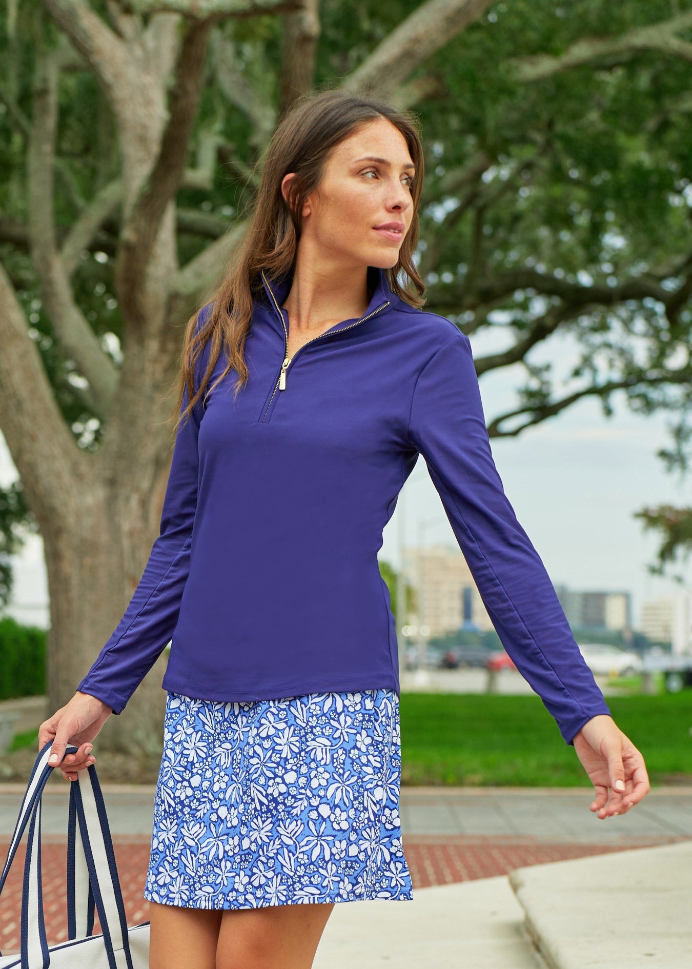 Woman wearing a purple long-sleeve top and blue floral skirt outdoors.