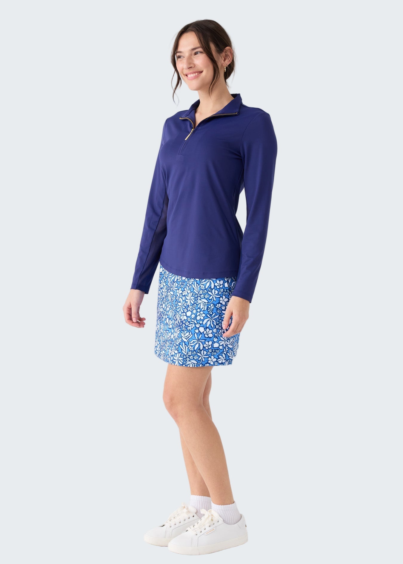 Woman wearing a blue long-sleeve top and floral skirt on a white background