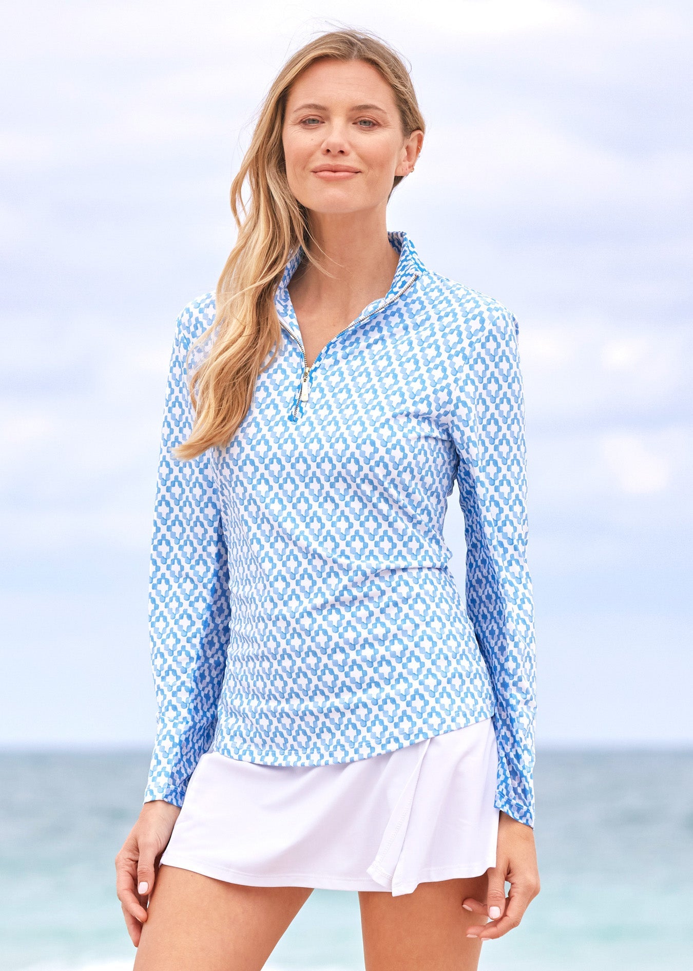 Woman wearing a blue and white patterned long-sleeve shirt and white shorts on a beach.