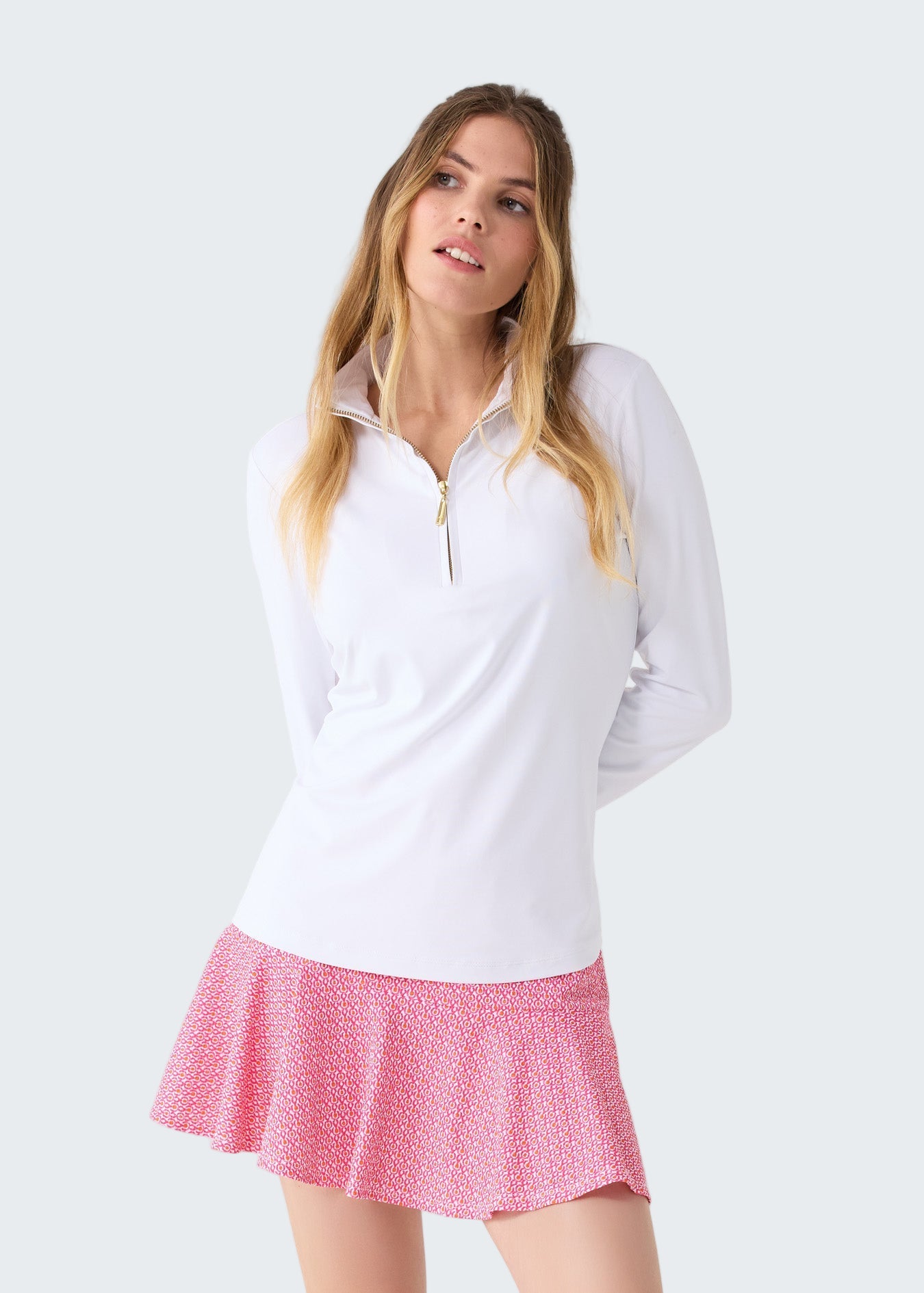 Woman wearing a white long-sleeve top and pink skirt on a white background