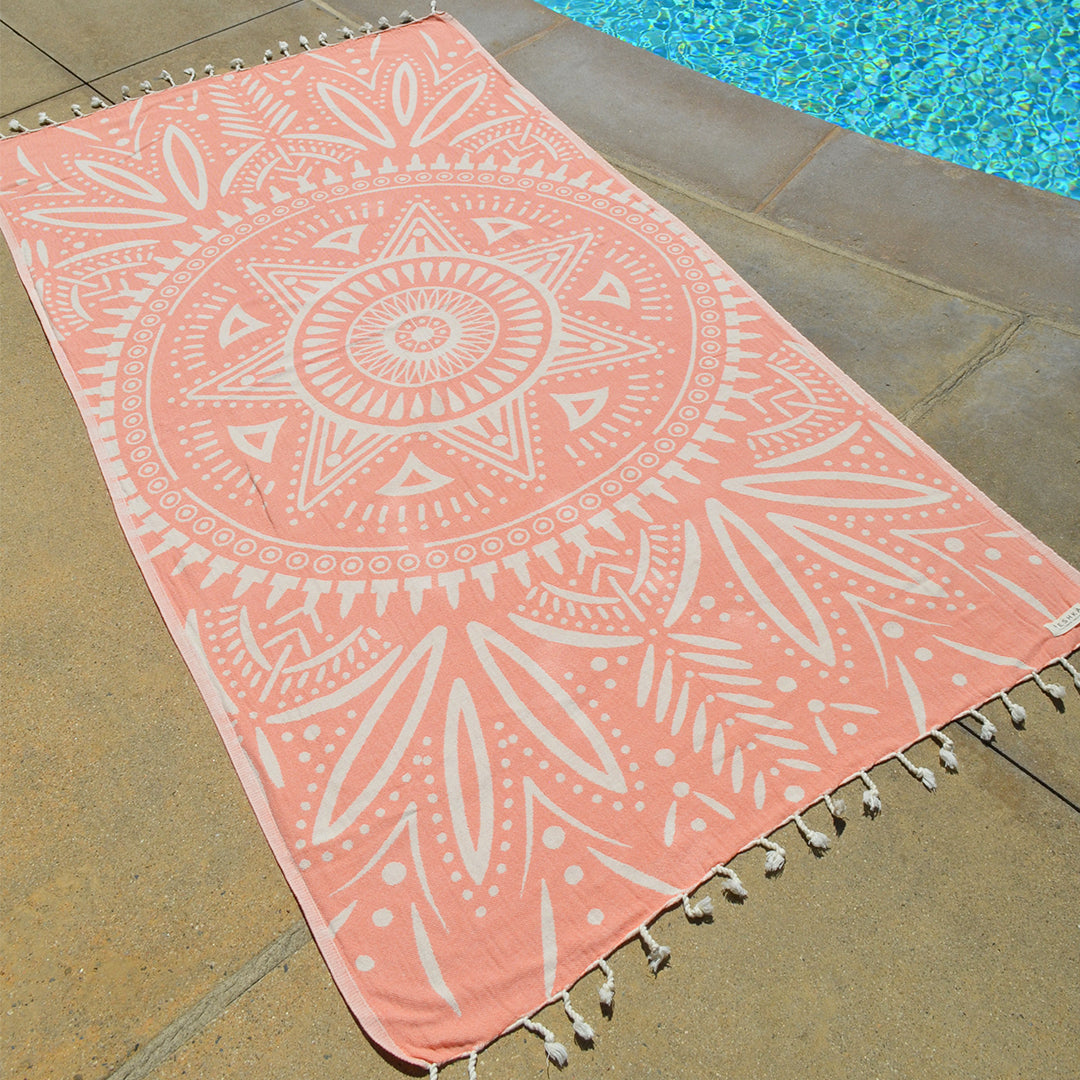 Pink and white patterned towel with tassels on a stone surface near a pool.