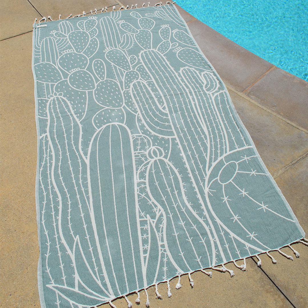 Teal towel with cactus pattern on a poolside floor