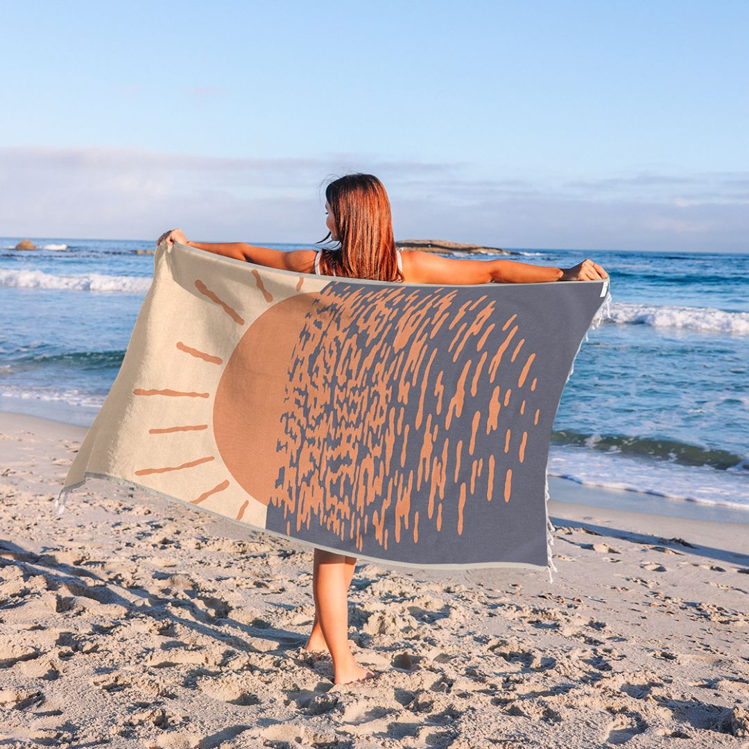 Person holding a beach towel with sun design on a sandy beach.