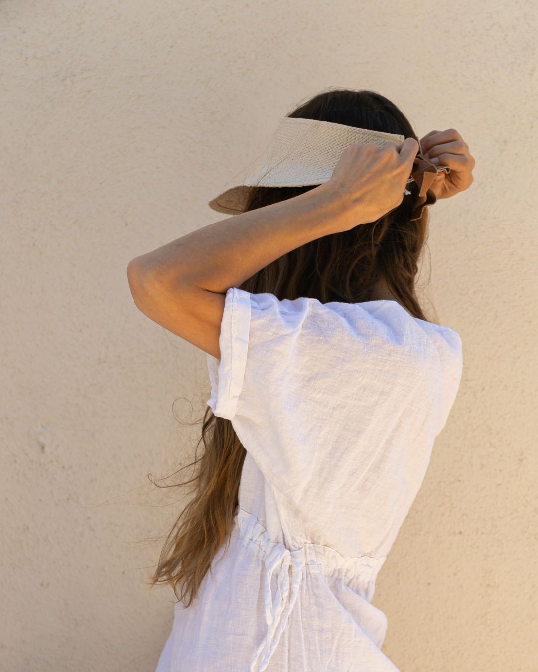 Woman wearing a white dress and visor against a beige wall