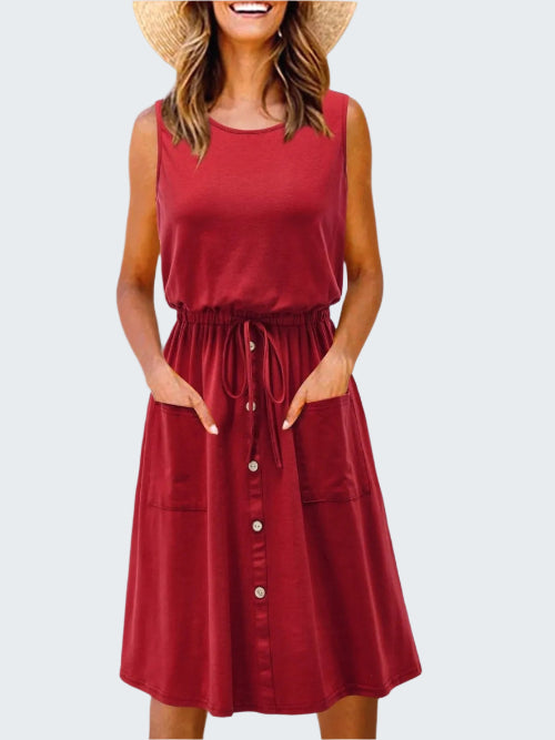 A model wearing a red sleeveless knee-length dress with a round neckline, drawstring waist, and front pockets.