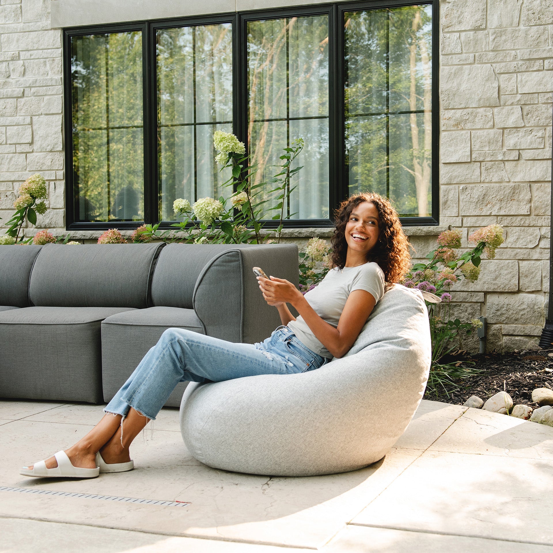 Woman sitting on a bean bag chair in a modern outdoor setting with a stone wall and large windows.