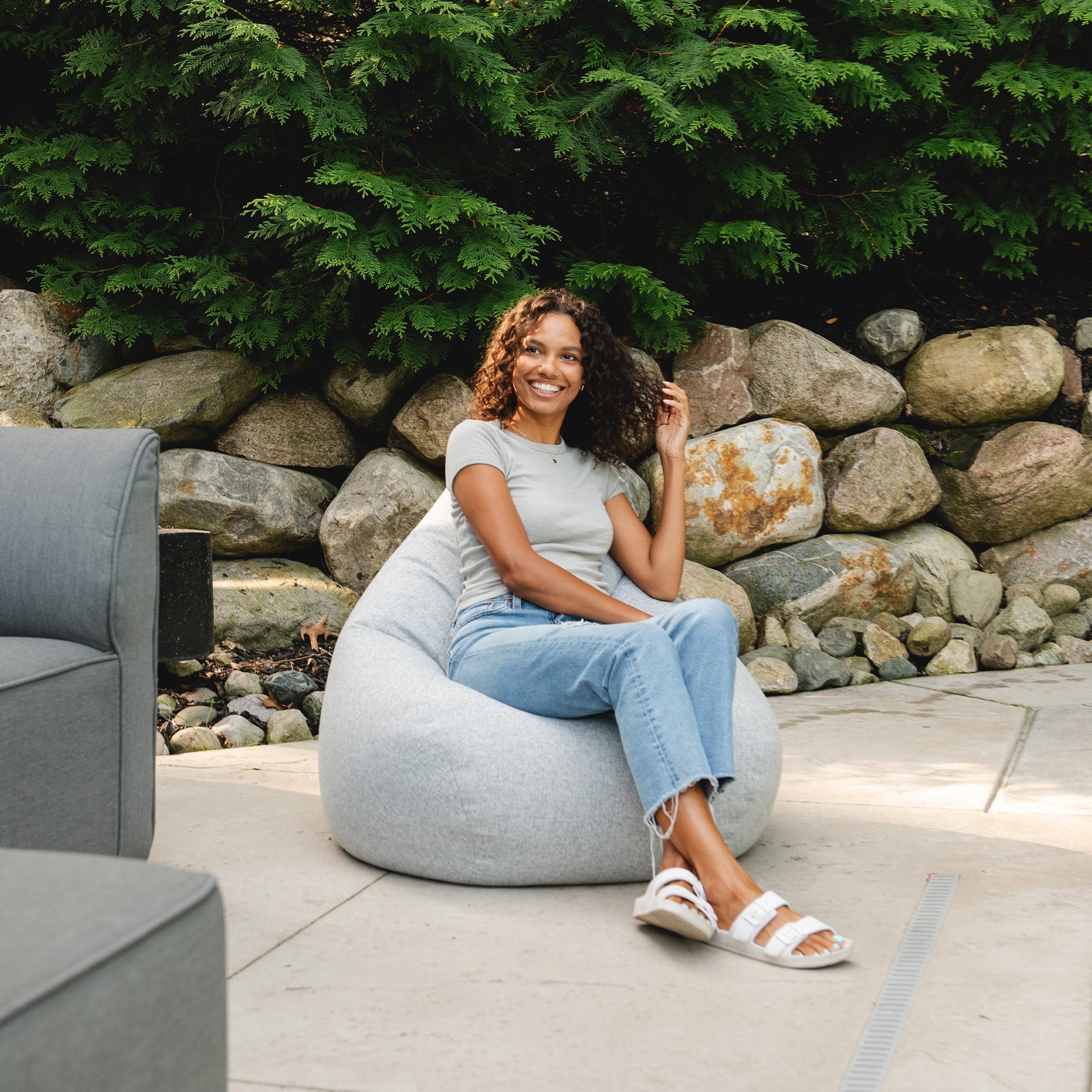Woman sitting on a bean bag chair outdoors with a stone wall and greenery in the background
