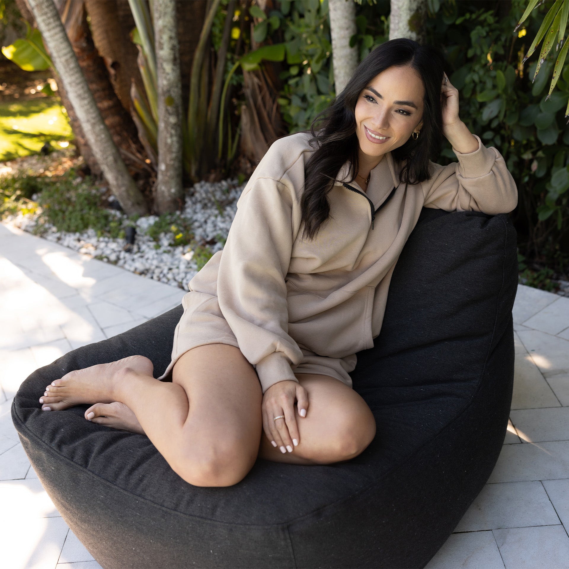 Woman sitting on a black bean bag chair outdoors with greenery in the background