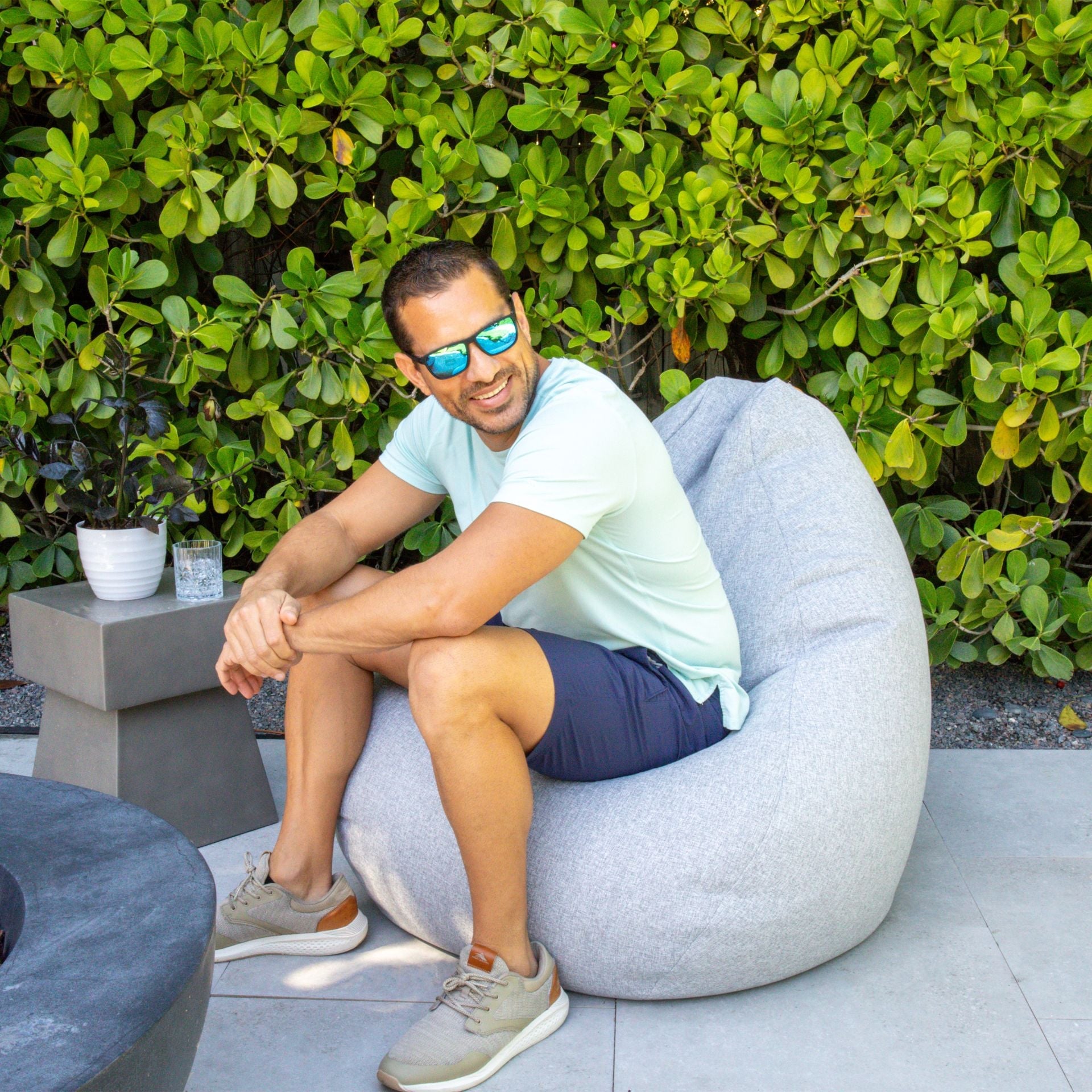 Man sitting on a bean bag chair outdoors with greenery in the background
