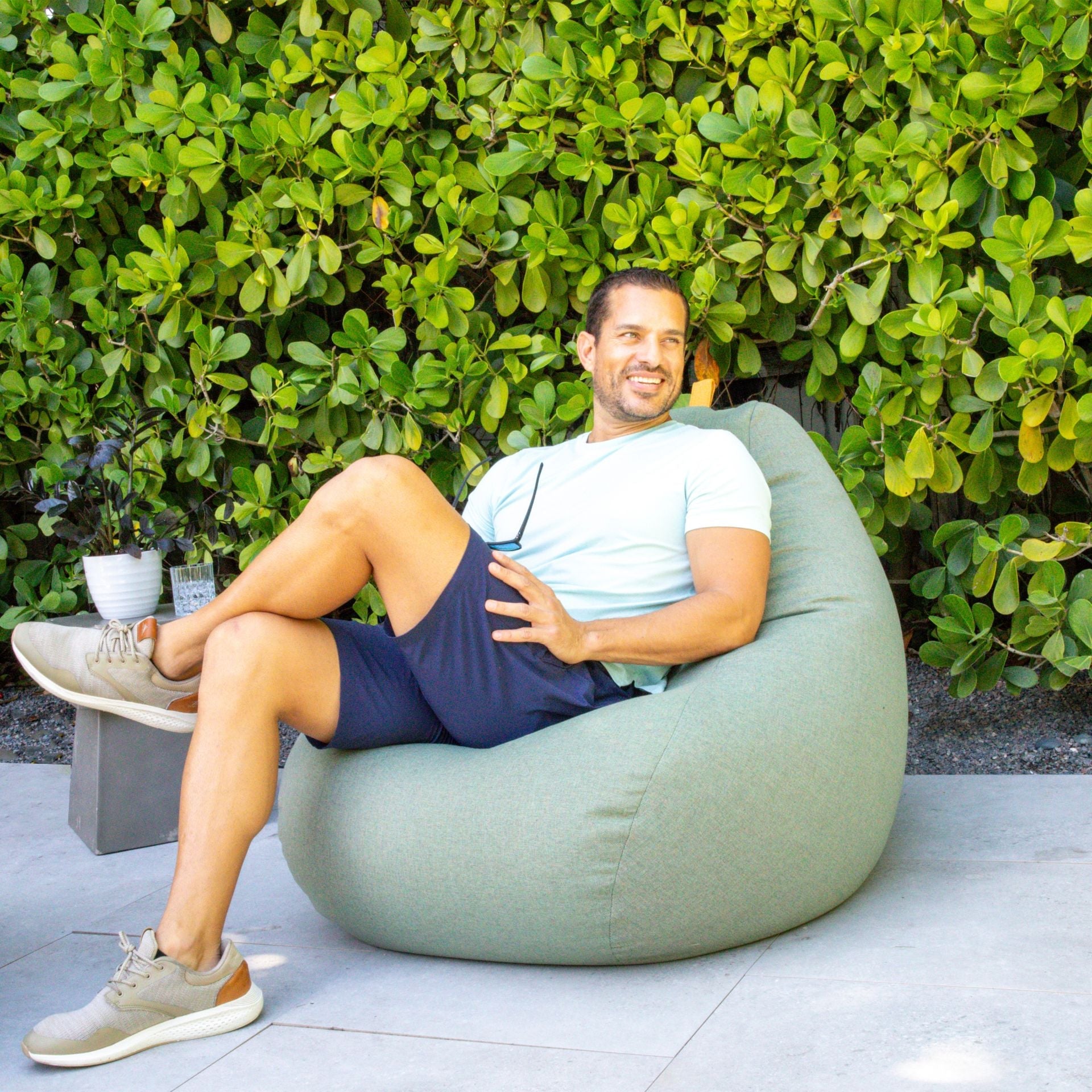 Man sitting on a green bean bag chair outdoors with greenery in the background