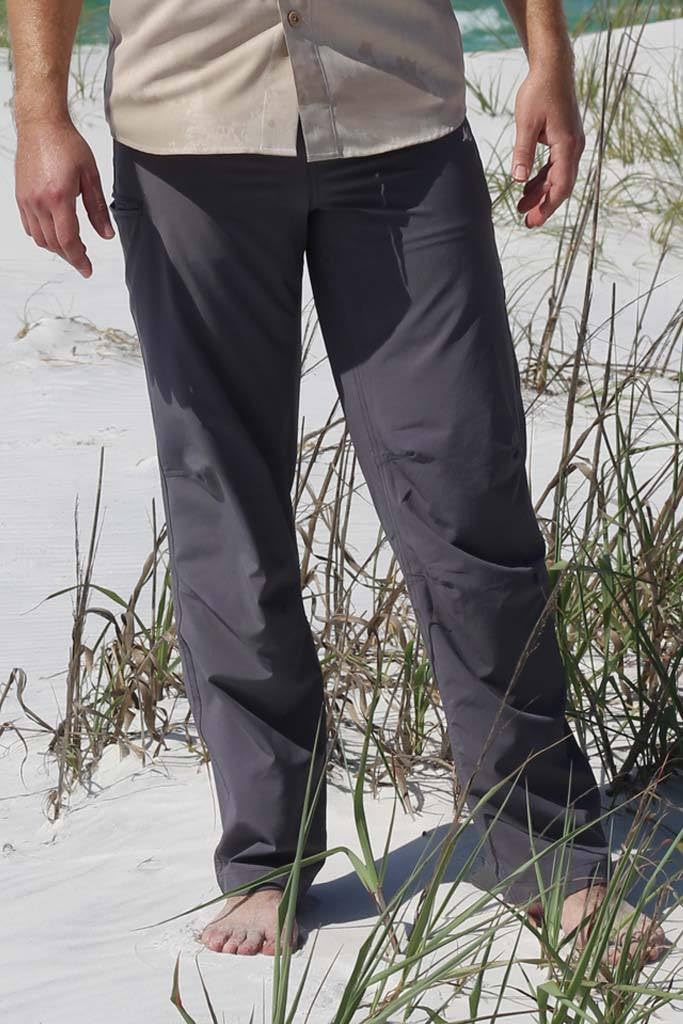 Person wearing dark pants standing on a sandy beach with grass.