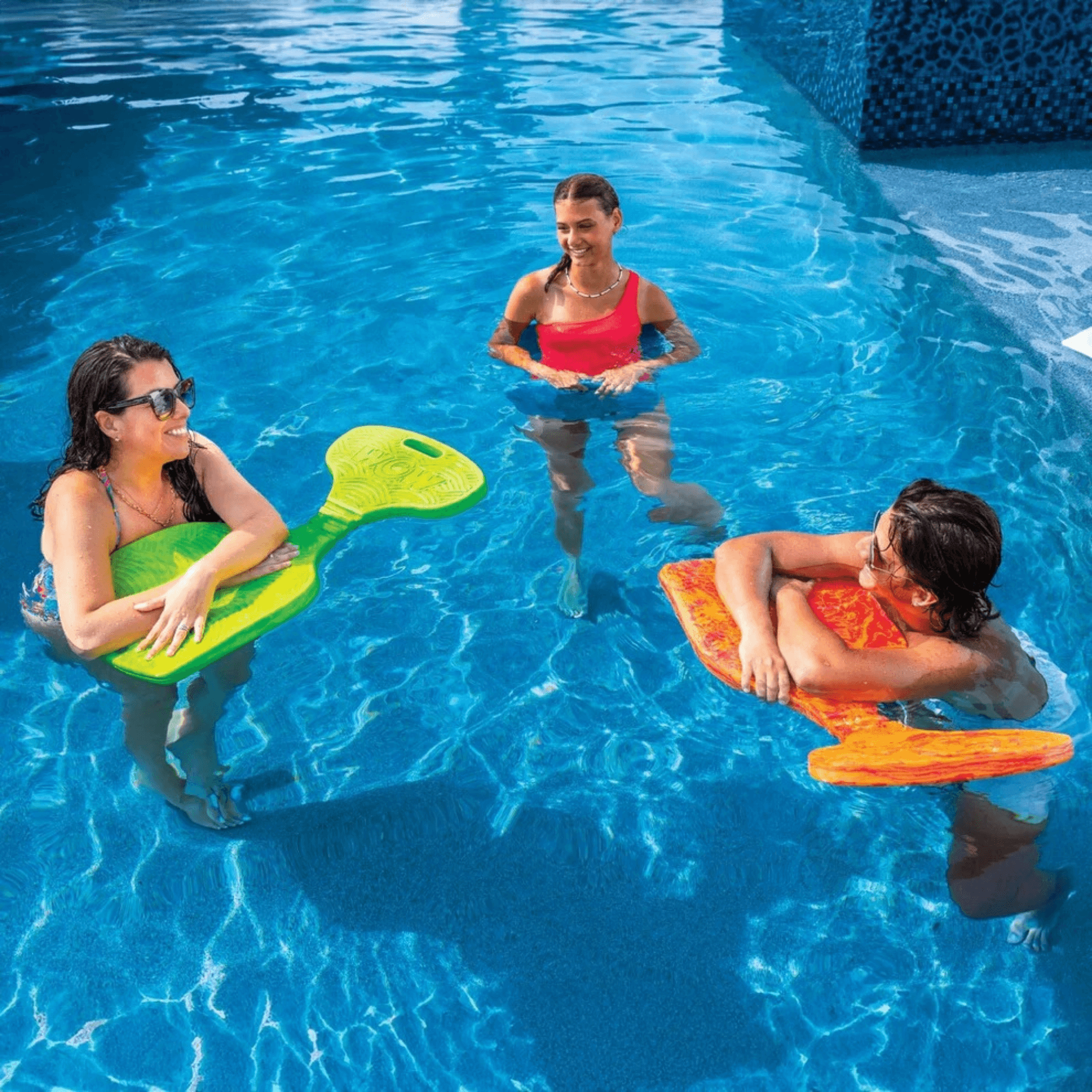 Three women in a pool with green and orange pool floats.