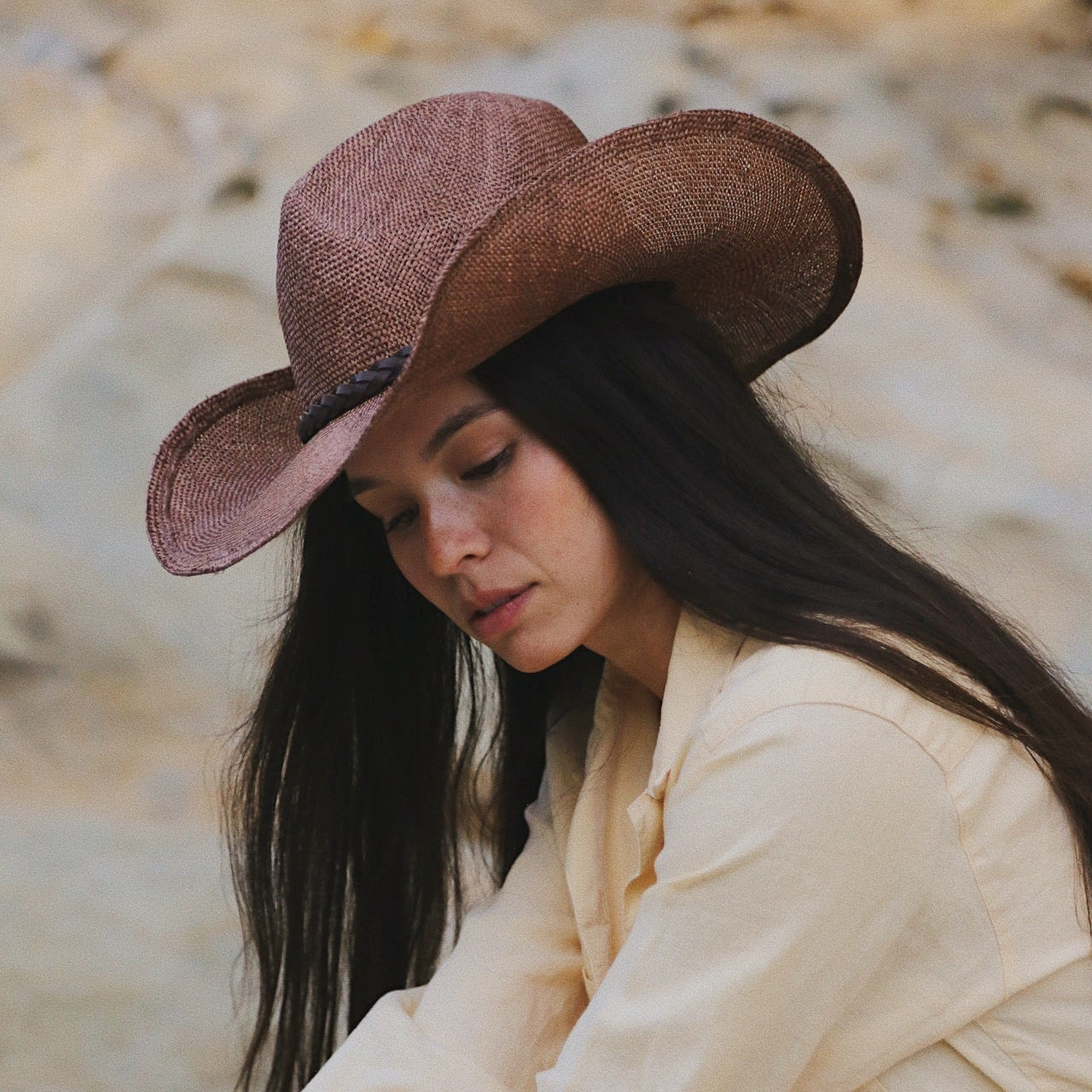 Woman wearing a brown cowboy hat and beige jacket outdoors