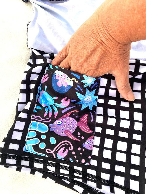 Hand holding a colorful fabric with fish and crab designs on a black and white checkered background.