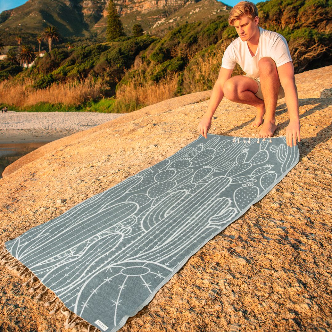 Person holding a towel with a nature design on a rocky beach
