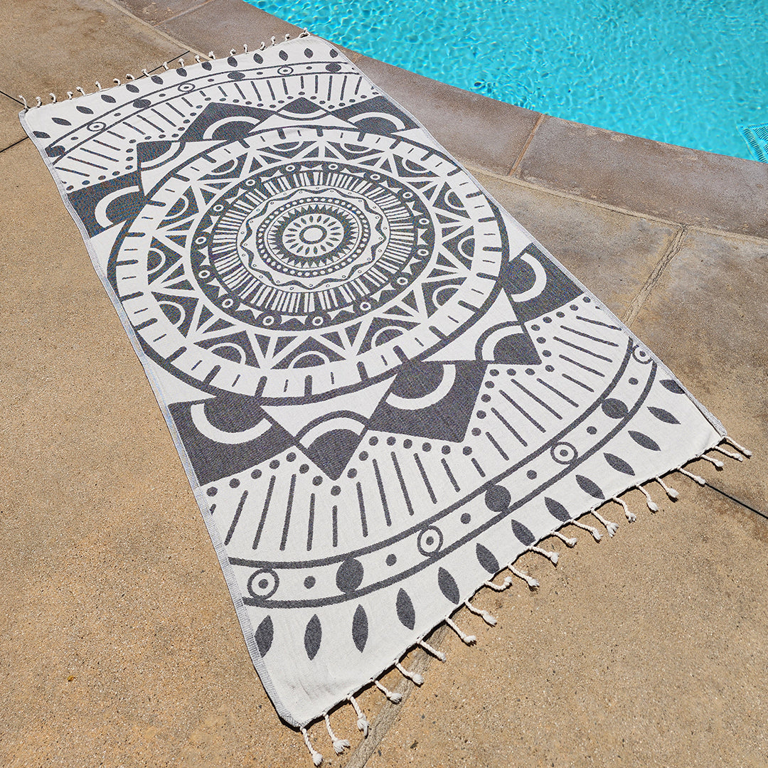 Decorative black and white patterned towel on a stone surface near a pool.