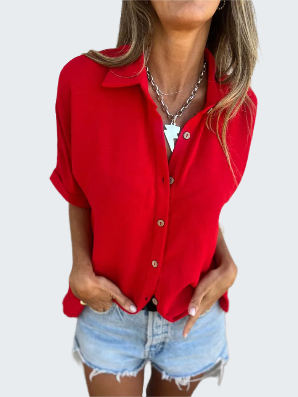 A person wearing a red collared neck half sleeve shirt paired with blue denim shorts, accessorized with a silver necklace.