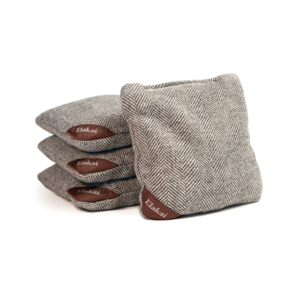 Set of four gray herringbone patterned cornhole bags with brown leather patches on a white background.