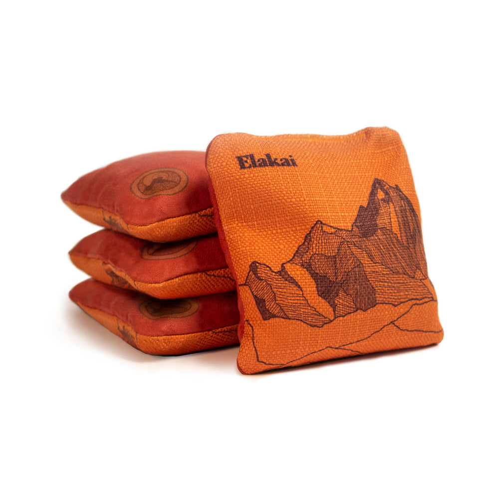 Orange cornhole bags with mountain design and 'Elakai' branding on a white background