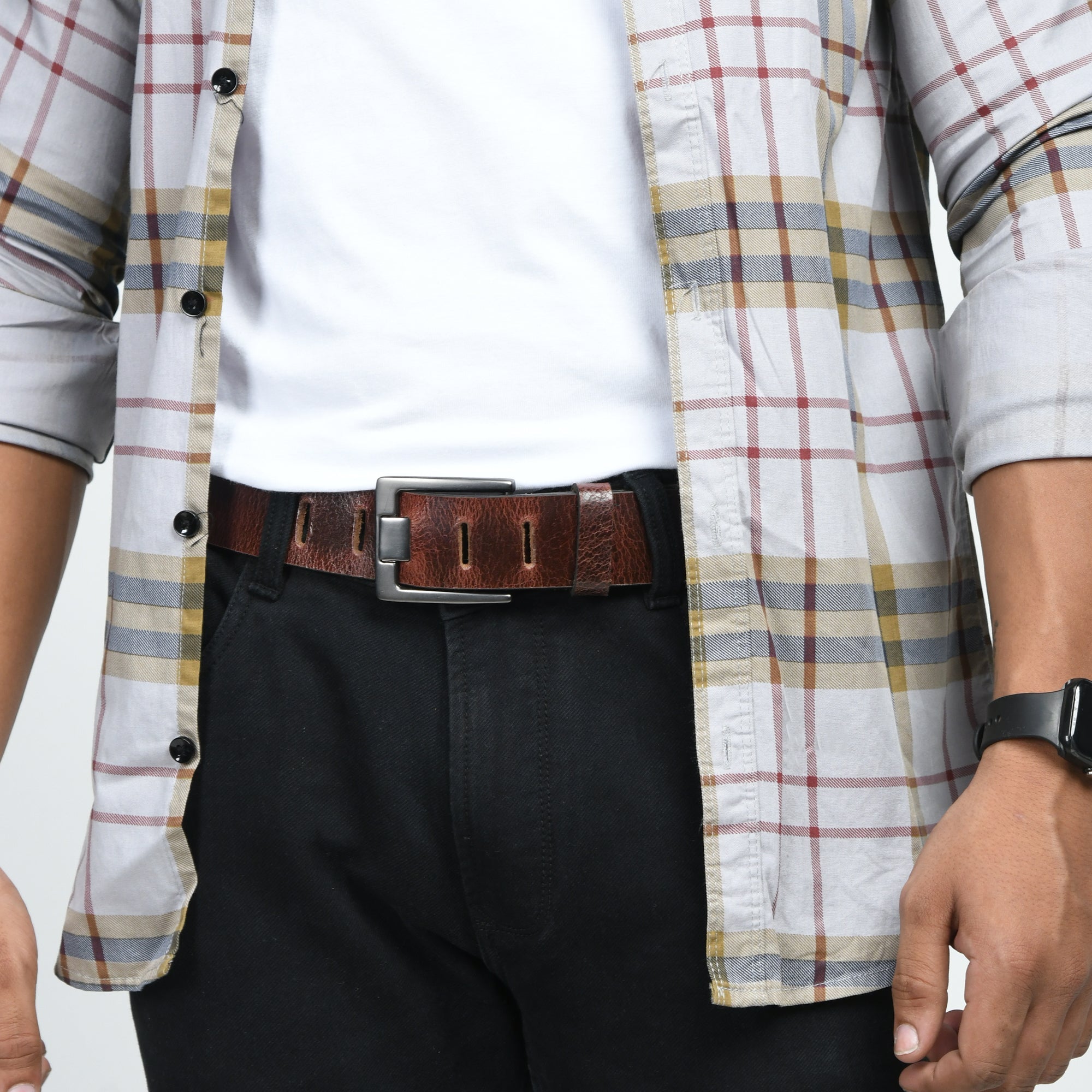 Person wearing a plaid shirt over a white shirt with black pants and a brown belt.