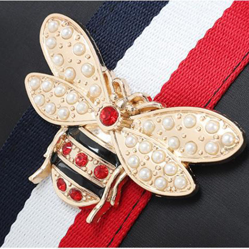 Gold bee-shaped brooch with pearls and red stones on a striped background