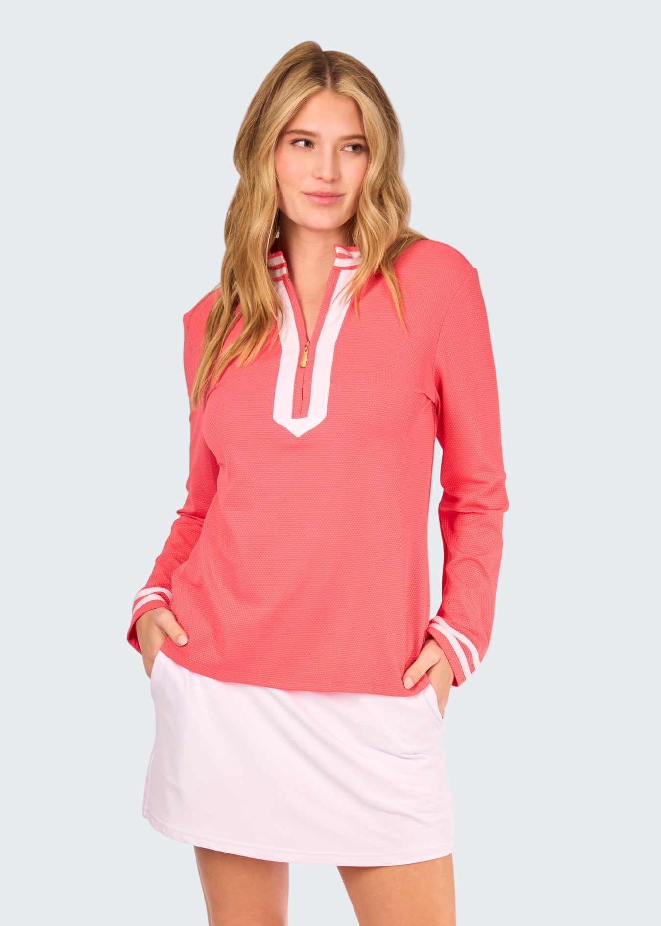 Woman wearing a coral long-sleeve top with white trim and a white skirt on a white background