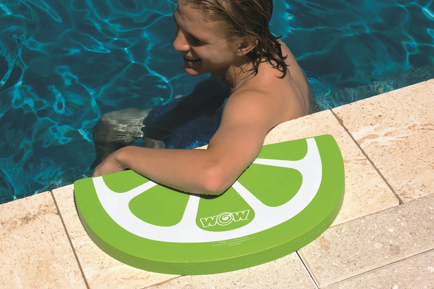 Child using a lime-shaped pool float with 'WOW' branding by a pool.