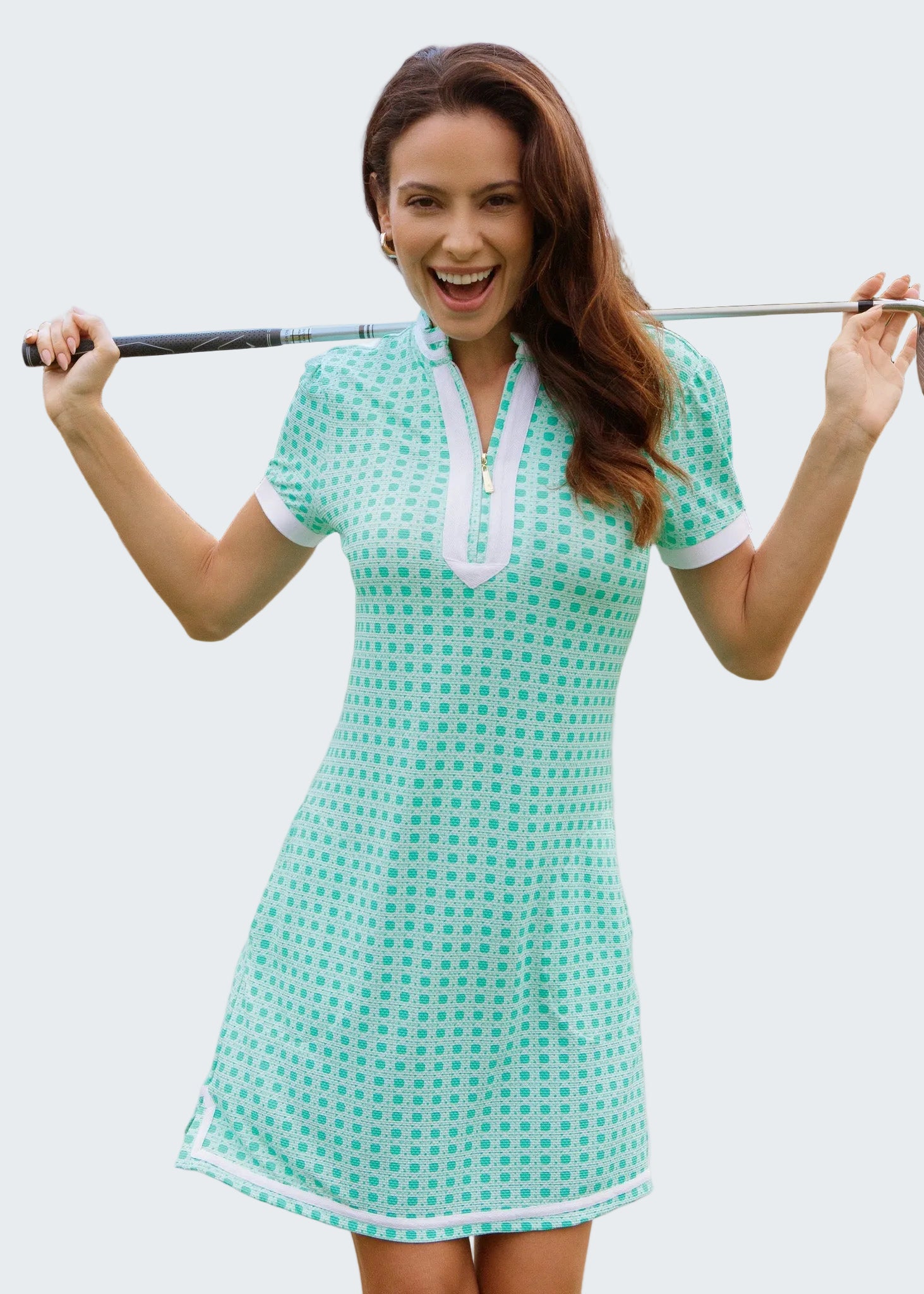 Woman in a green checkered dress holding a golf club on a golf course