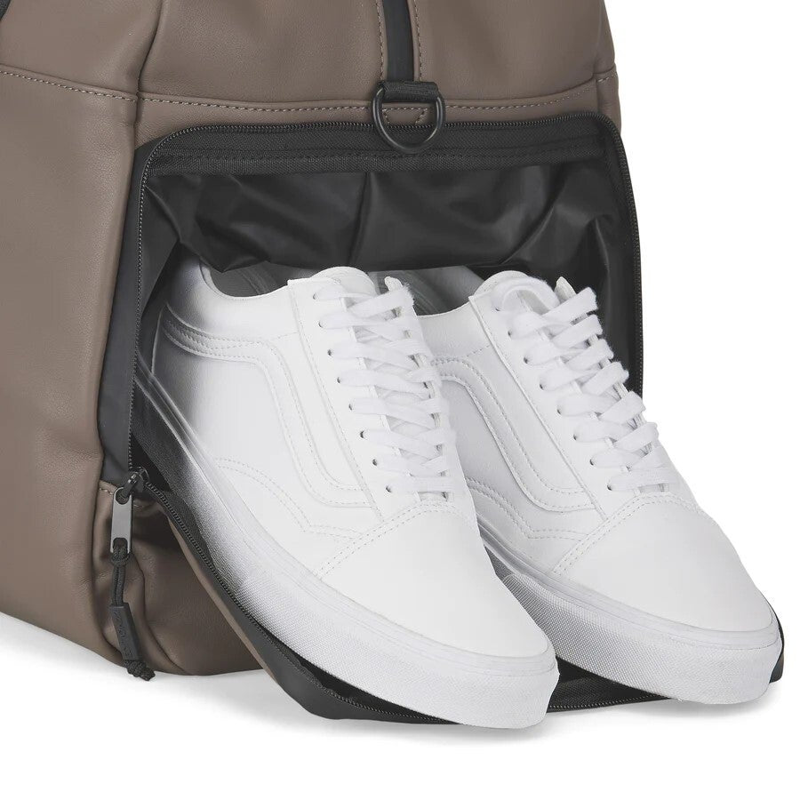White sneakers being placed into a brown backpack.