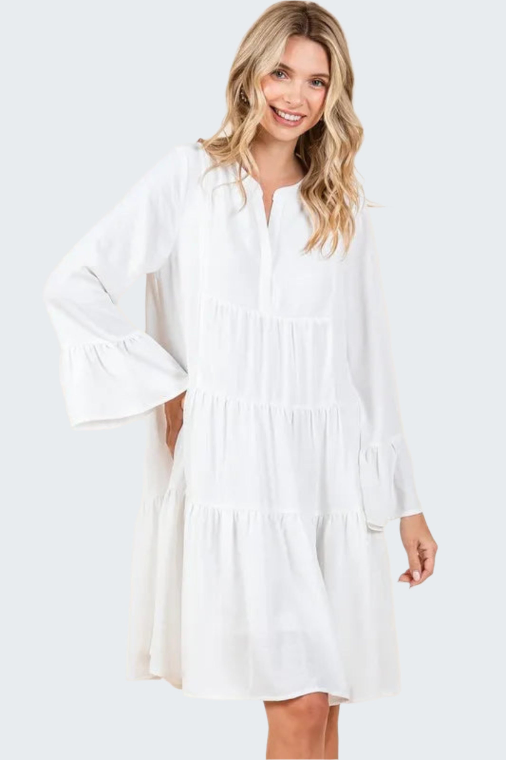 A woman wearing a white tiered notched flare sleeve dress with a V-neckline and long sleeves.