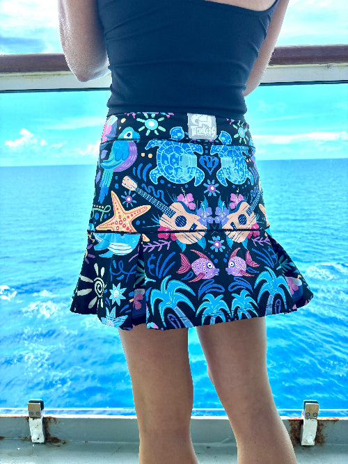 Person wearing a colorful skirt with sea-themed designs by a body of water.