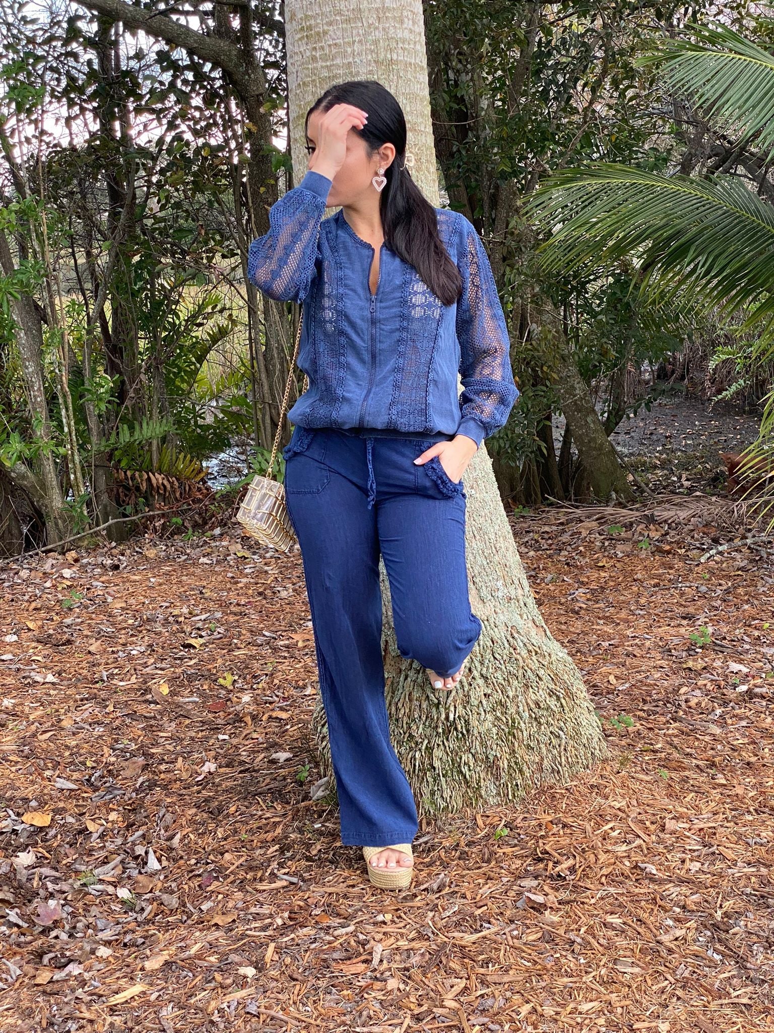Person wearing a blue outfit standing next to a tree in a natural setting
