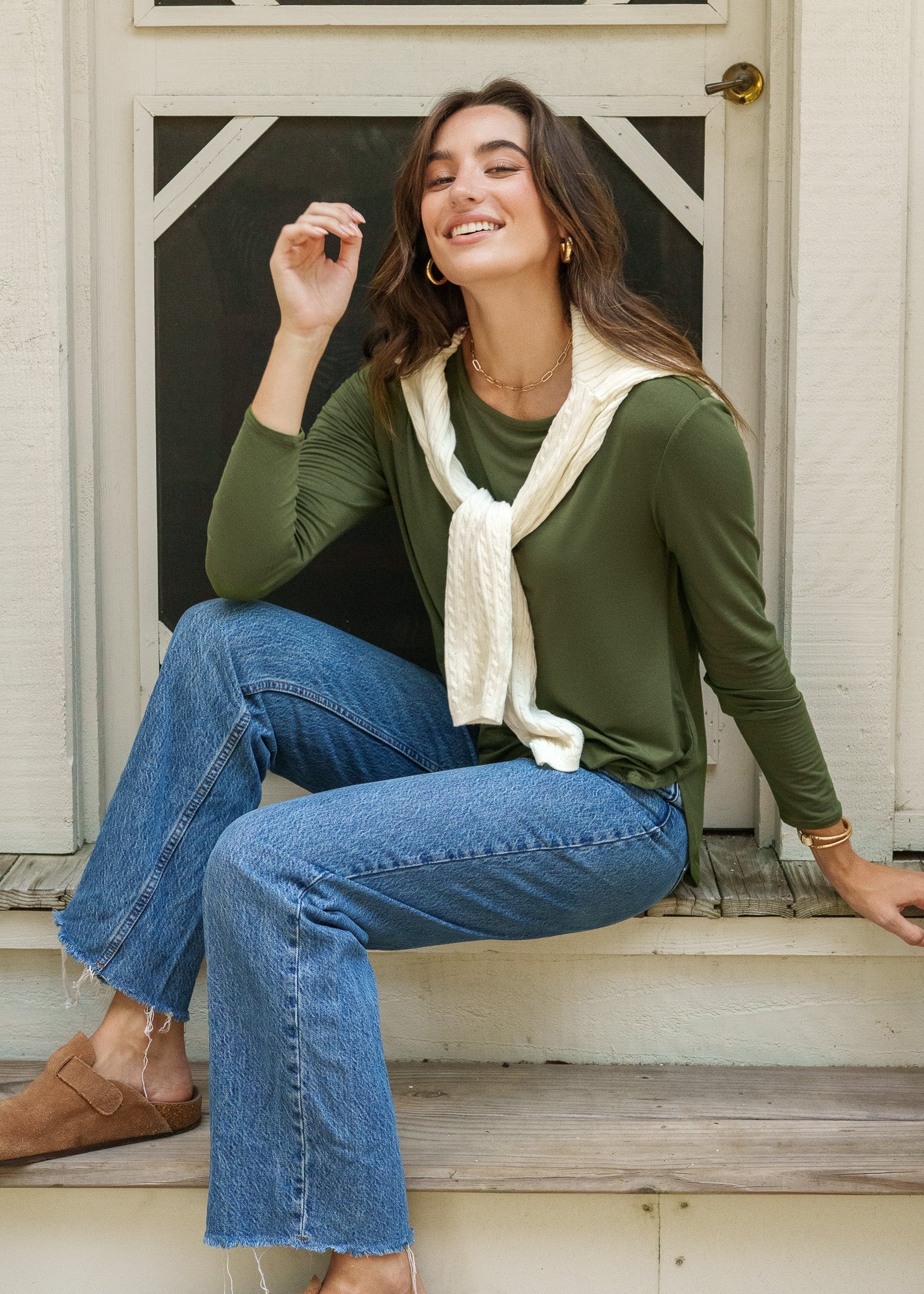 Woman sitting on steps wearing a green top, blue jeans, and a beige scarf.
