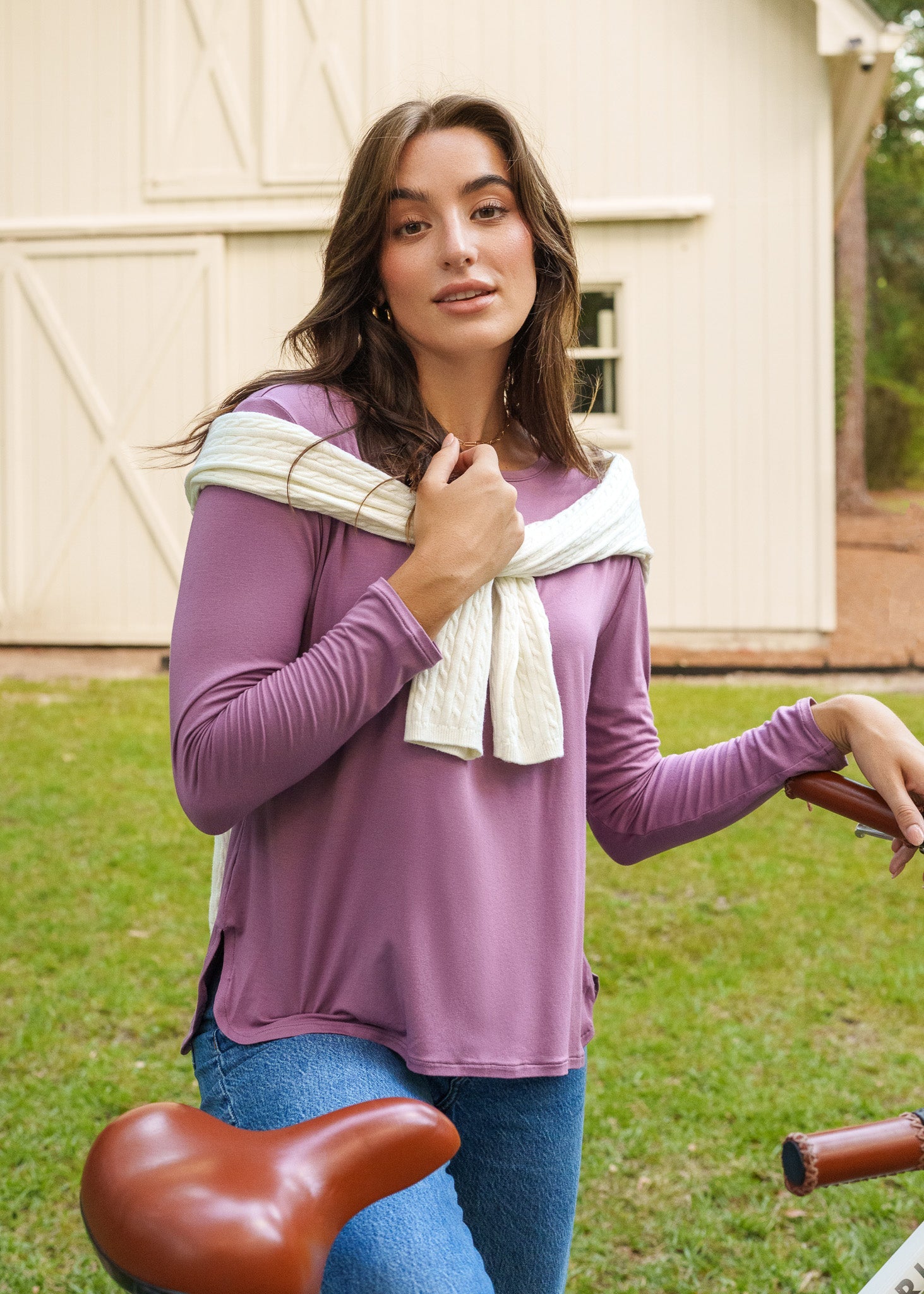 Woman in a purple shirt standing outdoors with a barn in the background