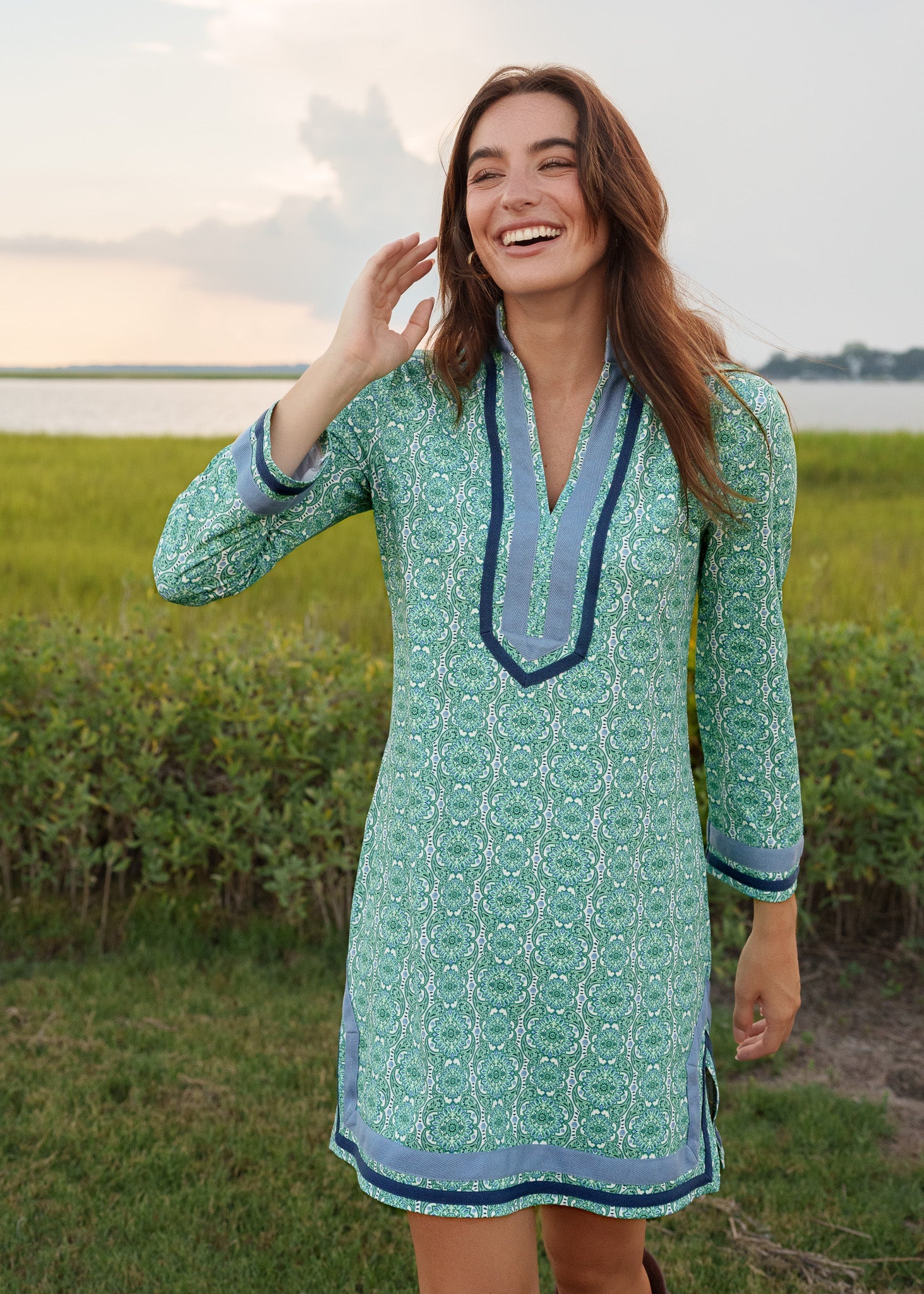 Woman in a green patterned dress standing in a field with a sunset in the background